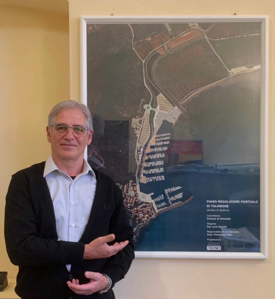 l'assessore all'urbanistica e al patrimonio, Luca Teglia con alle spalle il piano regolatore per il porto di Talamone